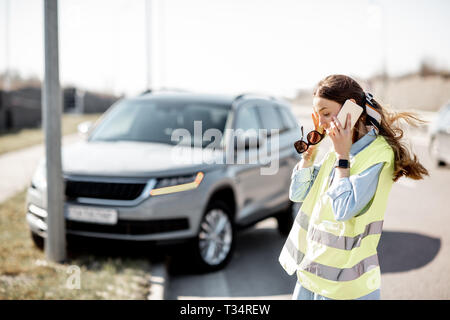 In imbarazzo donna che chiama assistenza stradale in piedi vicino alla macchina durante l'incidente stradale in autostrada Foto Stock