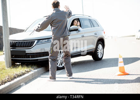 Assistenza stradale lavoratore aiutando giovane donna di uscire dal ciglio della strada dopo l'incidente sull'autostrada Foto Stock