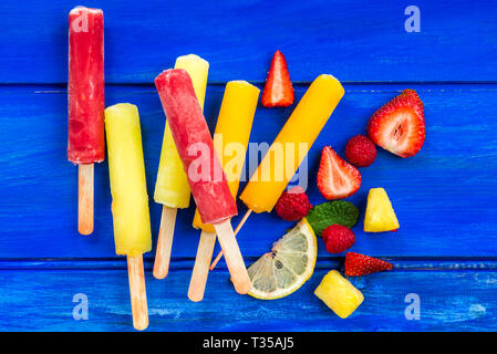 Arancio brillante, fragola e limone Popsicles ghiaccio sul legno sfondo blu Foto Stock
