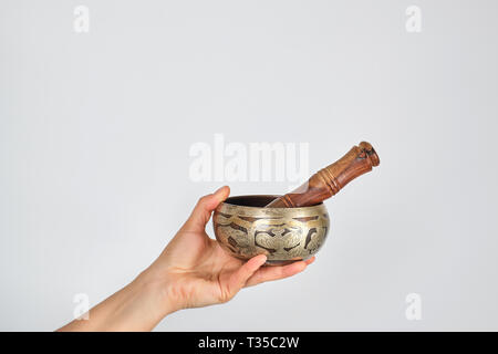 Il rame Singing Bowl e bastone di legno in mano femmina su sfondo bianco Foto Stock