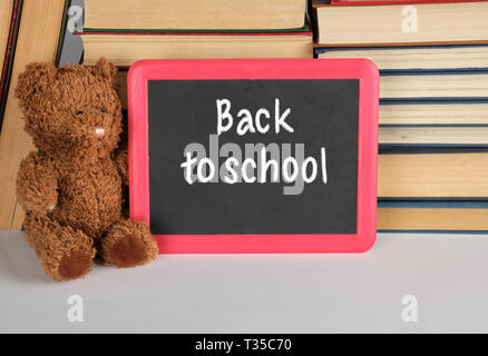 Brown Teddy bear e svuotare la scheda di colore nero con cornice rossa sullo sfondo della pila di libri, concetto si torna a scuola Foto Stock