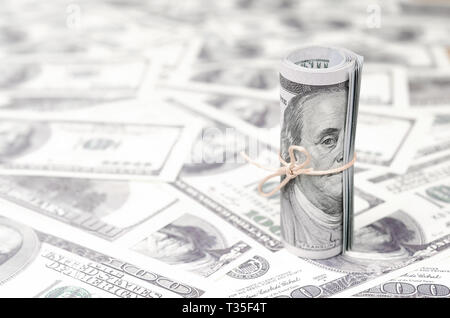 US dollari arrotolata e serrato con band giace su un sacco di banconote americane con sfondo sfocato. Grandi quantità di denaro Foto Stock