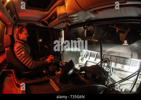 Una vista dalla cabina come un uomo aziona un gatto delle nevi la preparazione di piste da sci di notte francesi nella località alpina di Courchevel, Savoie. Gatto delle Nevi. Foto Stock