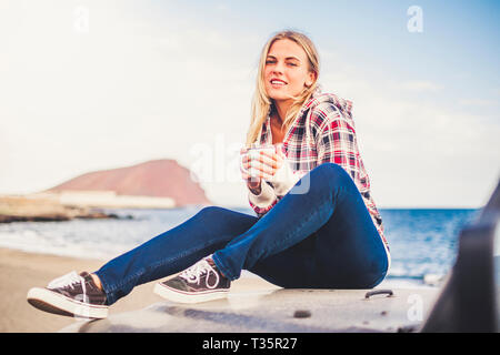 Allegro bella bionda tourist sedersi sulla sua auto nera e godetevi le attività outdoor sentimento della natura - il giovane viaggiatore persone con vista oceano e m Foto Stock