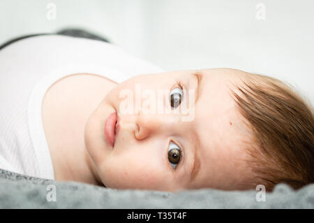 Adorabile bionda baby stare sdraiato sulla schiena sul letto bianco di guardare direttamente la fotocamera. Foto Stock