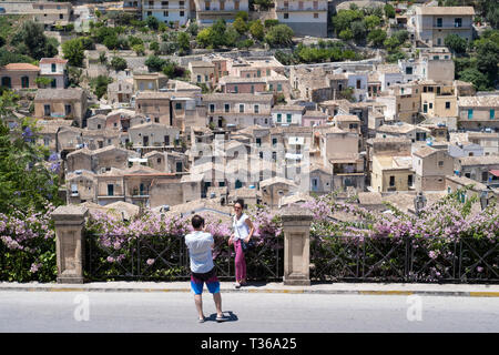 I turisti prendendo fotografie di souvenir su uno smartphone a Modica Alta con vista di Modica Bassa e architettura barocca, Sicilia Foto Stock