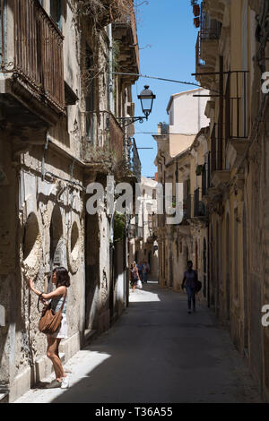 Scena di strada donna toccando il vecchio in pietra ornata vicoletto Via Dione in Ortigia, Siracusa, Sicilia Foto Stock