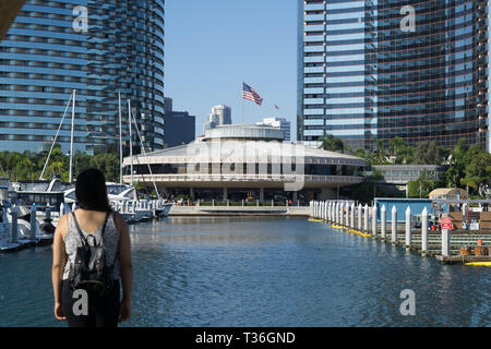 San Diego, CA / STATI UNITI D'America - 20 Giugno 2017: Donna guarda attraverso l'acqua per il Marriott e il ristorante 'Roy's" con la bandiera americana che si affaccia. Foto Stock