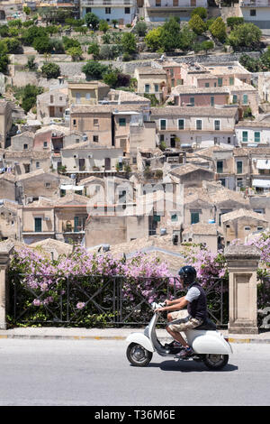 Uomo che cavalca scooter in hill città di Modica Alta guardando verso Modica Bassa, Sicilia, Italia Foto Stock