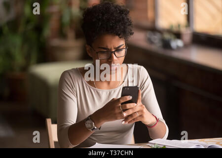 Sconvolto confuso donna africana azienda cellulare avendo problemi con il telefono Foto Stock