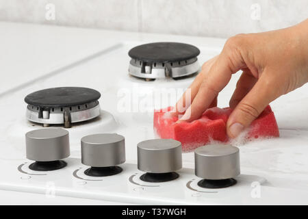 La mano della donna la pulizia della cucina a gas con spugna in cucina Foto Stock