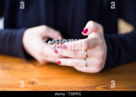 Donna in camicia nera digitando su smart phone in cafe, senza volto, close up, rosso dita, concetto di comunicazione Foto Stock