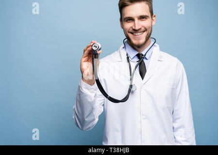 Bel giovane medic tenendo uno stetoscopio, isolato sulla luce blu. Foto Stock