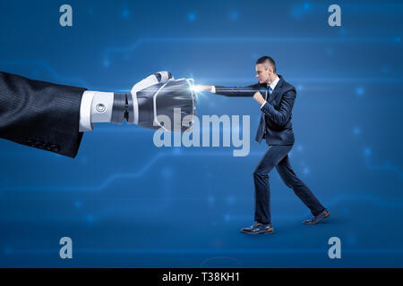 Vista laterale di imprenditore lotta contro la grande mano di robot, bianco lucido scintilla che appare al posto dove si toccano. Foto Stock