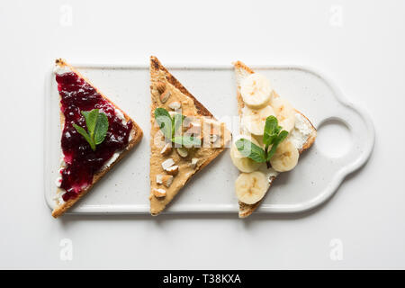 Diversi tipi di panini per una sana colazione per bambini senza zucchero, con dado pasta, banane, marmellata di frutti di bosco. Vista da sopra. Foto Stock