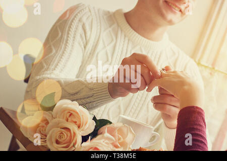 Giovane uomo mettendo sulla ragazza dito anello di fidanzamento pur avendo una cena romantica con fiori al caffè accogliente. Impegno di coppia giovane nell'amore. Gio Foto Stock