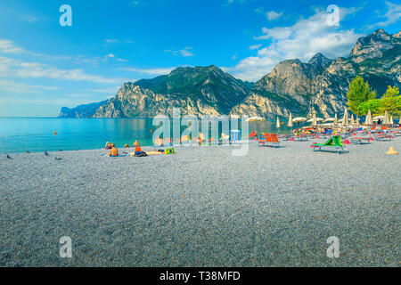Estate fantastica spiaggia di destinazione di vacanza. Sedie a sdraio con ombrelloni sulla spiaggia sul lago di Garda, Torbole, Italia, Europa Foto Stock