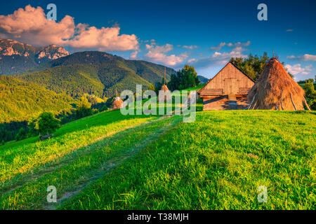 Bella estate paesaggio alpino paesaggio, balle di fieno con capanna in legno e le alte montagne sullo sfondo al tramonto, crusca, Transilvania, Romania, Euro Foto Stock