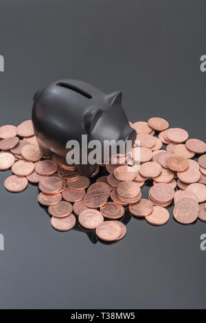 Ceramica Nera salvadanaio con monete del Regno Unito riflettente su sfondo nero. Metafora per il risparmio di denaro, risparmi personali, risparmiando spiccioli, British spiccioli. Foto Stock