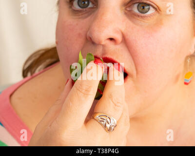 Una donna adulta con unghie rosse e le labbra di mangiare una fragola Foto Stock