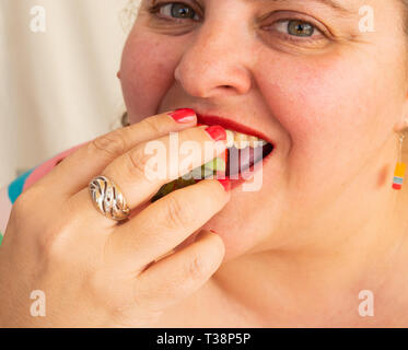 Una donna adulta con unghie rosse e le labbra di mangiare una fragola Foto Stock