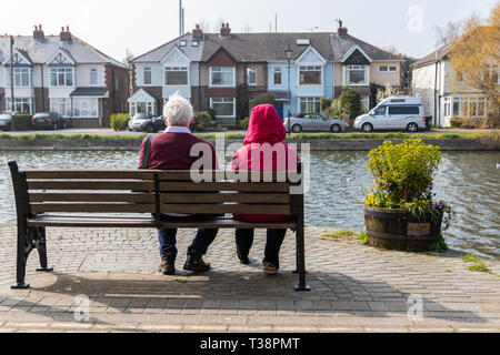 Coppia di anziani seduto su una panca in legno con vista sull'acqua Foto Stock