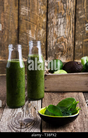 Verde Sano frutta e verdura frullati in bottiglie su tavola in legno rustico, spinaci, avocado, Apple, il sedano e il succo di lime drink con ingredienti, Foto Stock