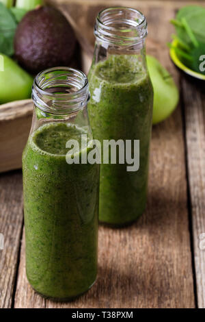 Verde Sano frutta e verdura frullati in bottiglie su tavola in legno rustico, spinaci, avocado, Apple, il sedano e il succo di lime drink con ingredienti, Foto Stock