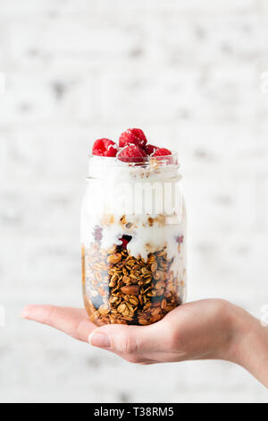 Cereali e yogurt con frutti di bosco in vaso su una donna mano. Concetto di perdita di peso e fitness Cibo, alimentazione sana ed equilibrata Foto Stock