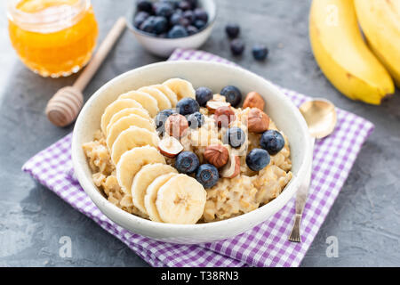 Farina di avena porridge con frutti banana, mirtilli e nocciole. Mangiare sano, dieta e perdita di peso concept Foto Stock