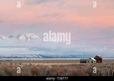 Vecchi fienili e case sopraffatte dal Monte Moran e i Teton Mountains in una nebbiosa mattina d'inverno. Il Parco Nazionale del Grand Teton, Wyoming Foto Stock