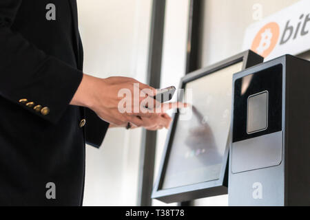 Imprenditore acquisto e trasferimento cryptocurrency per telefono cellulare dal bancomat per le operazioni di acquisto e di vendita cryptocurrency. Foto Stock