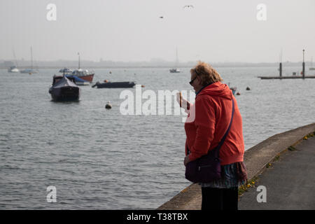 Centro anziana signora a mangiare il gelato dal mare con barche in background Foto Stock