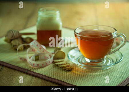 Succo di zenzero in una coppa trasparente e miele vaso collocato accanto con nastro di misurazione. Concetto di sano. Foto Stock