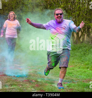 Grande Uomo sovrappeso runner ridendo e braccia tese essendo coperto di vernice sul cancro Macmillan carità 5K colore fun run. Foto Stock