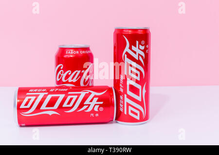 Peniscola , Castellon, Spagna - 07 aprile 2019 : tre lattine di coca cola, due scritto in cinese, bevande isolato su una luce sfondo rosa. La non-alcol Foto Stock