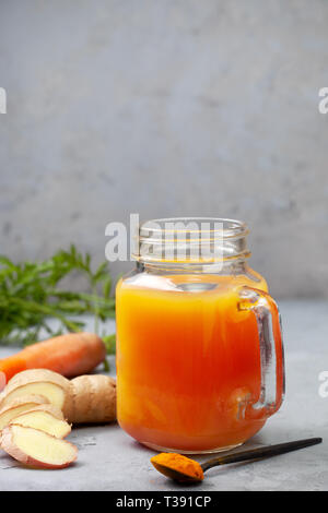 Detox drink. la carota, lo Zenzero Curcuma bere in un bicchiere su sfondo grigio. spazio copia Foto Stock