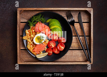 Frittelle di patate con salmone, uova, avocado e pomodori su una piastra nera su sfondo scuro. vista dall'alto. Foto Stock