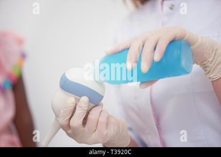 Close up medico donna mano che tiene in mano a indossare guanti di gomma, la sonda ad ultrasuoni e di gel di accoppiamento preparare per la diagnostica a bright armadio a Foto Stock