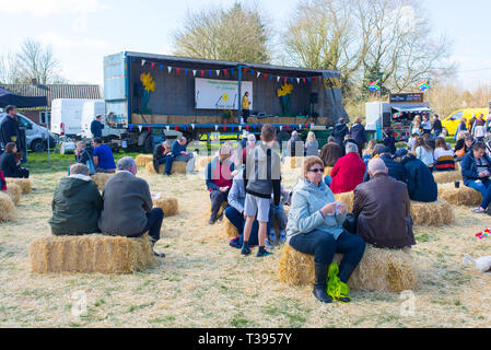 Thriplow, Cambridge, Inghilterra, Regno Unito - Marzo 2019: le persone che frequentano un locale country fair ascoltando musica dal vivo seduti su balle di fieno Foto Stock