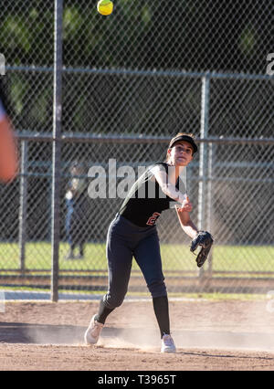 Adolescente di sesso femminile softball player in nero uniforme di gettare la sfera attraverso infield per la fuori in una nuvola di polvere. Foto Stock