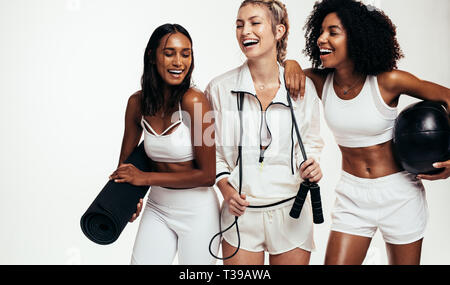 Allegro giovani multi-etnico amici femmina tenendo rottura dopo la sessione di allenamento. Gruppo diversificato le femmine in sportswear con materassino yoga, saltando la corda e me Foto Stock