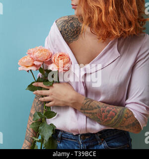 Una giovane donna con un tatuaggio tiene in mano un mazzo di rose rosa intorno a uno sfondo blu con copia spazio. La festa della mamma concept Foto Stock