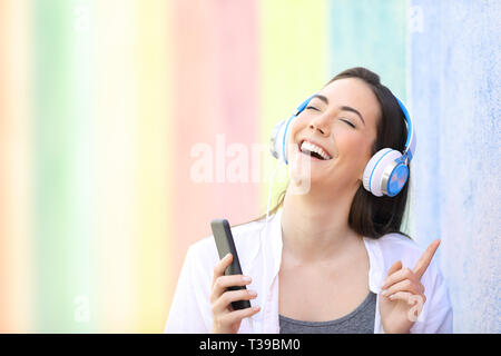 Felice ragazza cantare ascoltando musica con smart phone in un colorato street Foto Stock