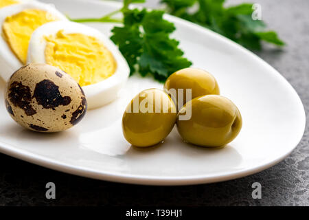 Bollito di uova di gallina con uova di quaglia, olive e prezzemolo sulla piastra bianca, cibo sano Foto Stock