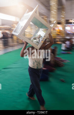 L'uomo posizionando la donazione scatole la mattina presto all'interno del Chauk Htat Gyi Pagoda Tempio del 65 metro lungo Buddha reclinato immagine, Yangon,Myanma Foto Stock