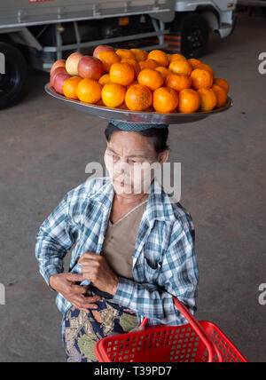 Donna birmano con thanaka face painting che porta una piastra con la frutta in testa alla stazione degli autobus di Kinpun Vlllage,Kyaiktiyo,Myanmar. Foto Stock