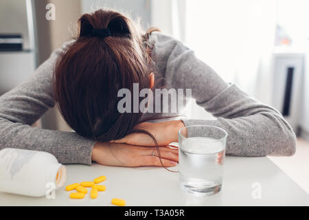 Giovane donna arrabbiato e stanco di assunzione di pillole contro la malattia in cucina. Donna che piange a causa della depressione. La sanità e la medicina concept Foto Stock