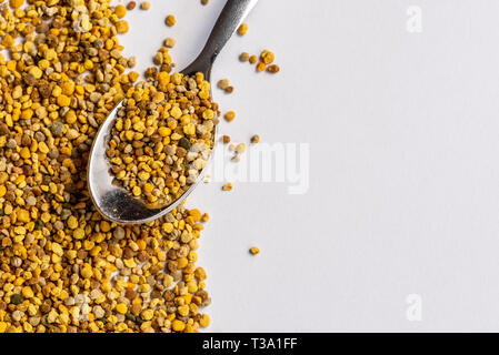 Granuli di polline di api su un foglio di carta bianca con un cucchiaino da caffè di granuli, copyspace Foto Stock