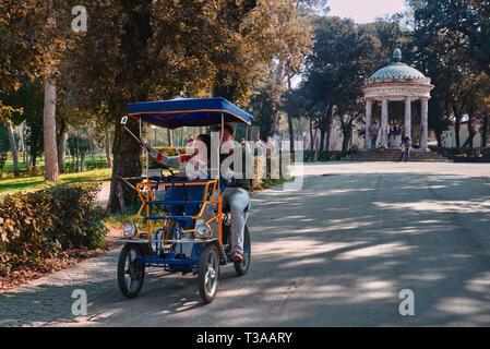 Roma, Italia, 19 febbraio 2019, Villa Borghese, un giovane uomo, donna, prendere un selfie durante la guida di una macchina elettrica, Tempio di Diana in background sul ri Foto Stock